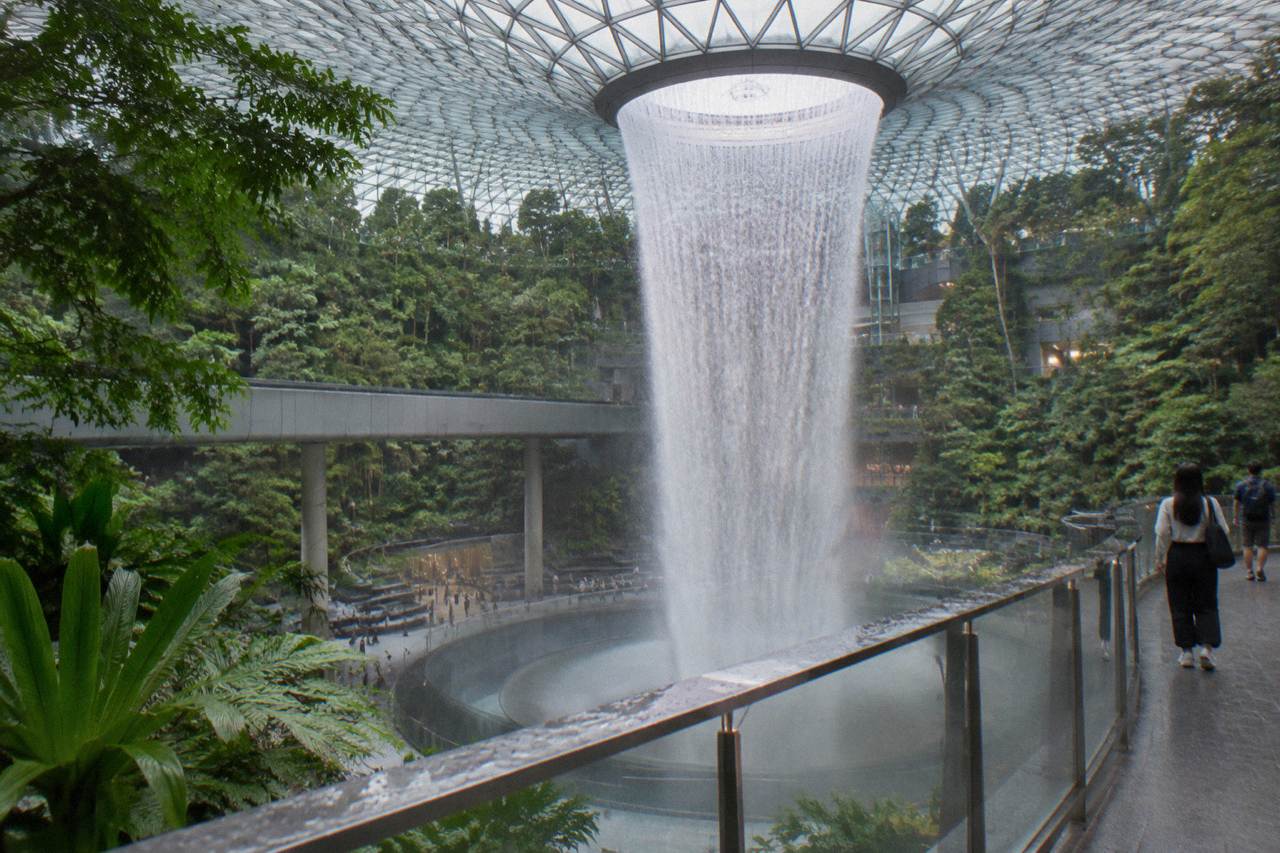 The Rain Vortex waterfall falling through the centre of Jewel Changi Airport, ringed by forest planting and walkway levels