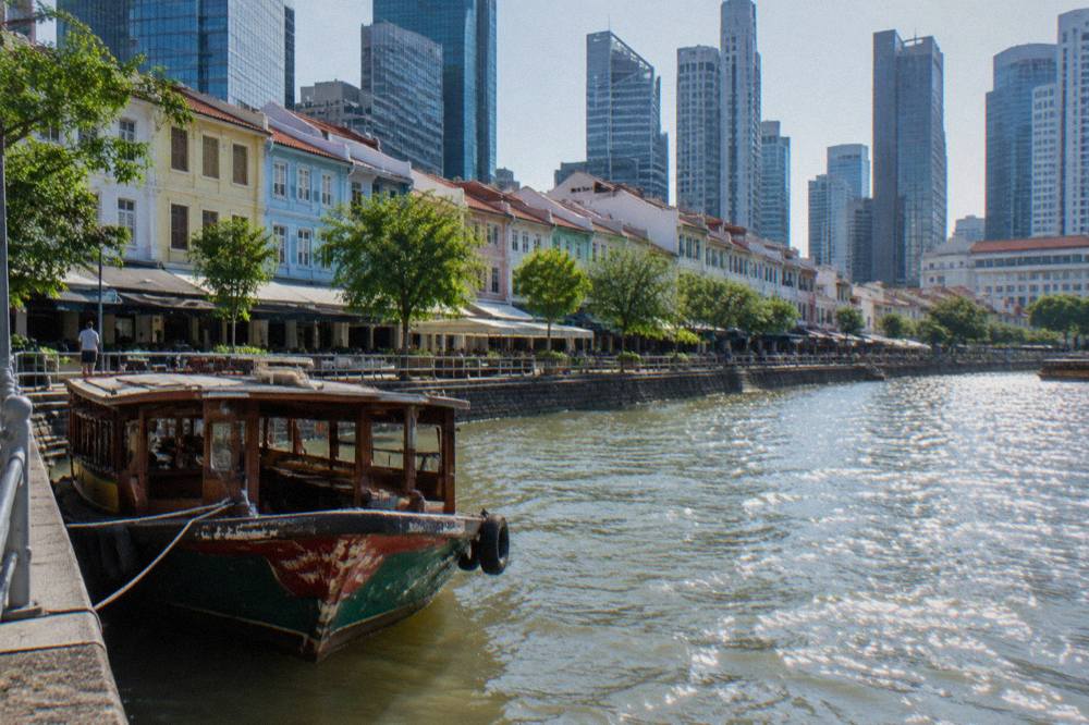 The Singapore River with historic shophouses and modern skyscrapers reflected in the water.