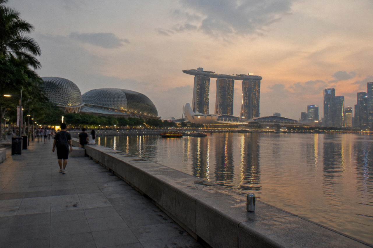 Waterfront promenade at Marina Bay with illuminated towers reflected in the water after dark