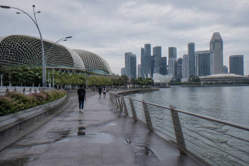 Waterfront promenade curving around a bay with tall towers on the opposite shore