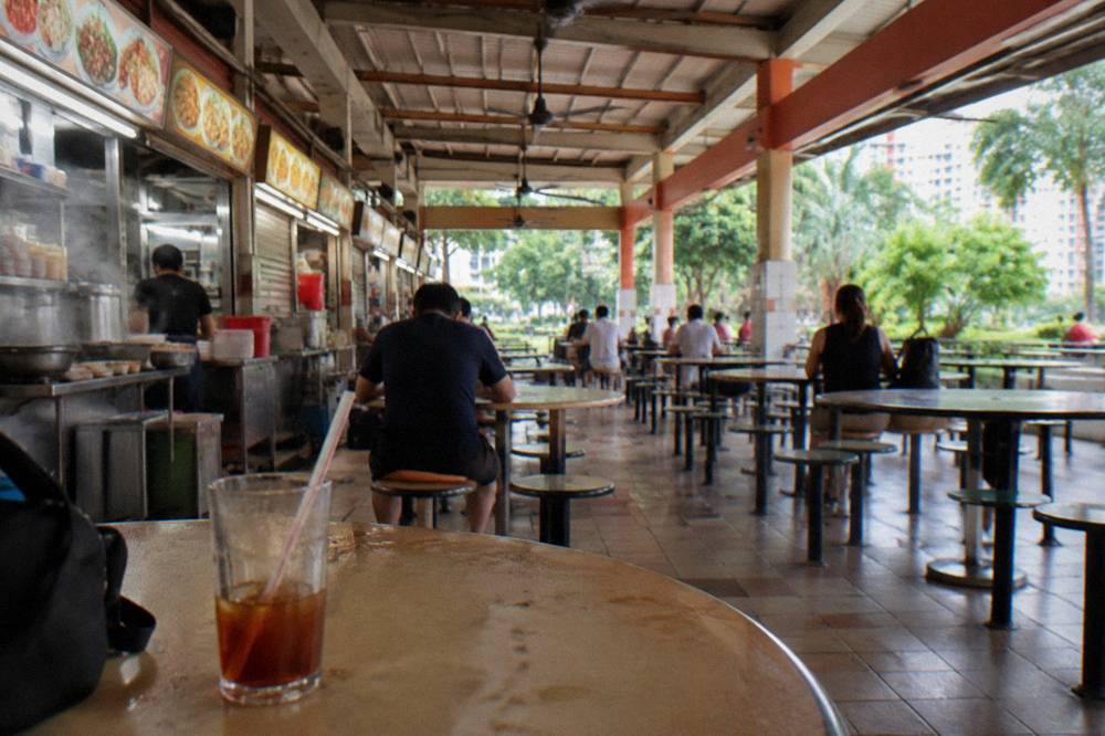 Rows of food stalls with hanging signs inside a sheltered hawker centre