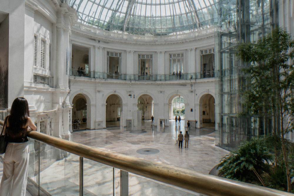 A tall museum atrium with a glass ceiling and marble floor