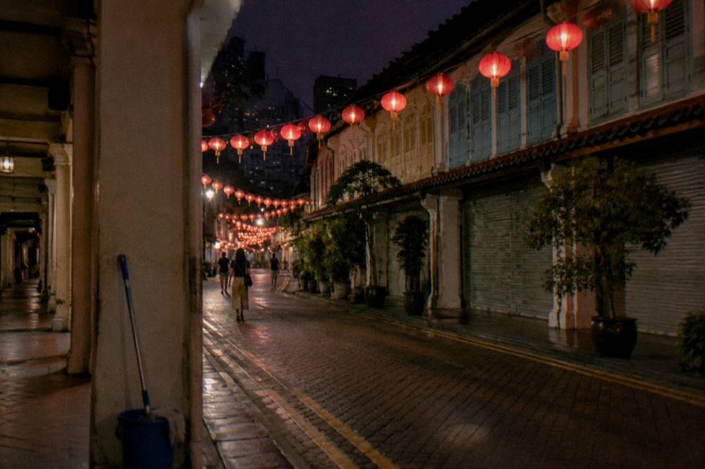 Red lanterns strung across a narrow street above closed shutters and lit signs