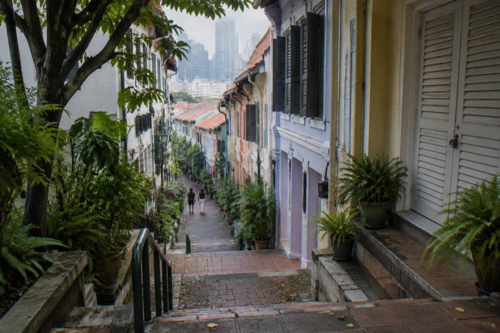 A narrow Chinatown street with rows of traditional shophouses under a daytime sky