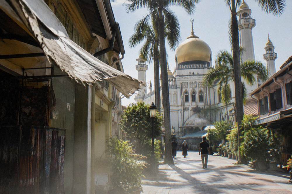 A mosque with a golden dome and minarets above low shopfronts