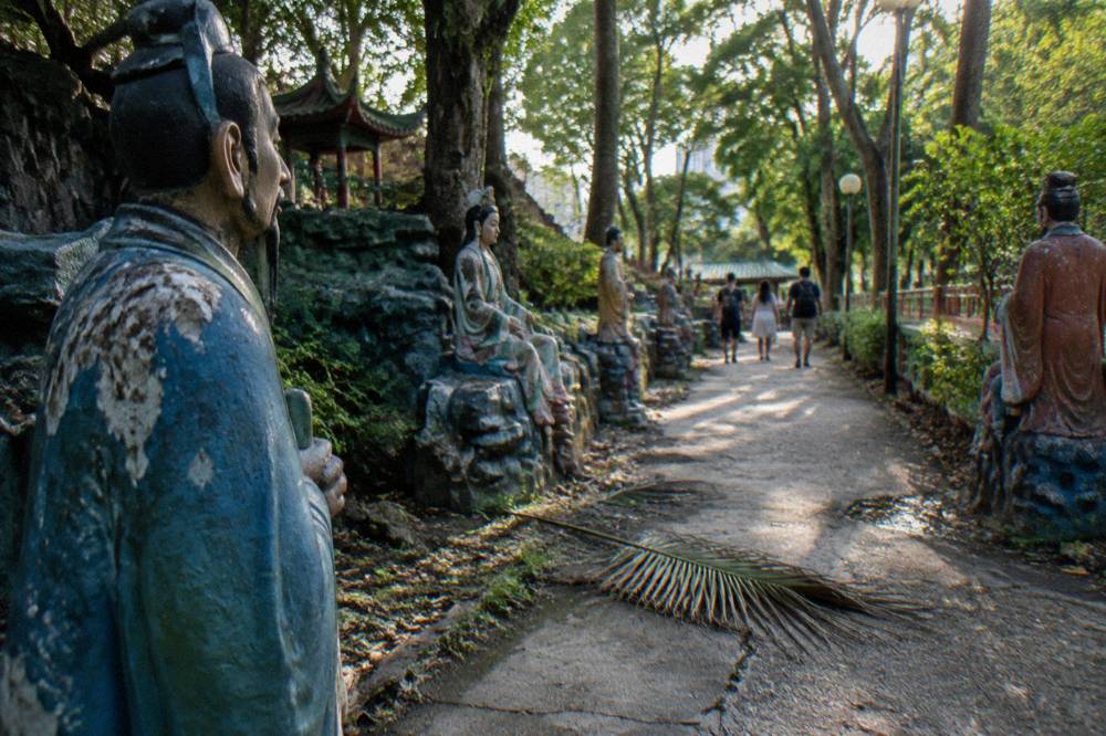 A garden walkway lined with colourful statues of mythological figures under trees