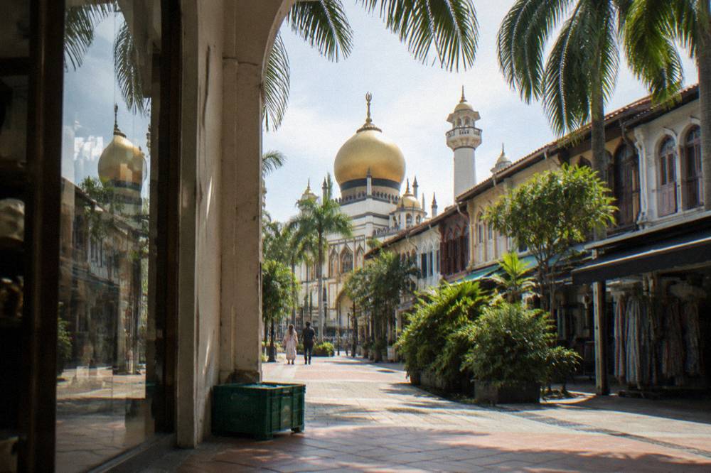 Golden dome and minarets of a mosque rising above shopfronts in daylight