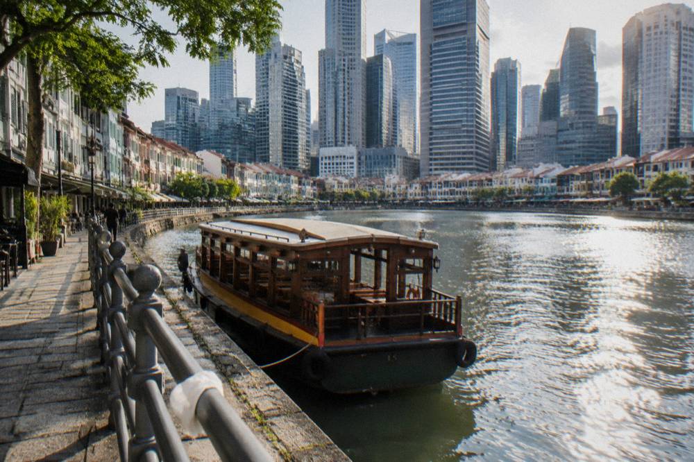 A riverside promenade with old shophouses on one bank and towers on the other