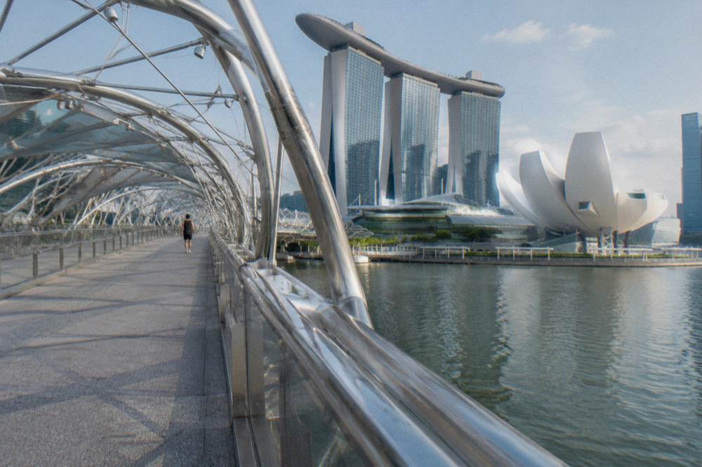Helix Bridge curved walkway over water with city towers and a museum building beyond