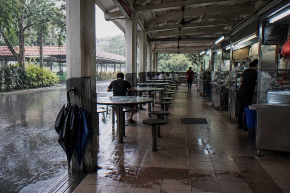 Shared tables and stall counters under bright lights inside a covered hawker centre